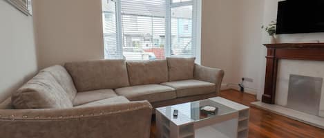 A living room with a beige sofa, a glass coffee table, and a fireplace.
