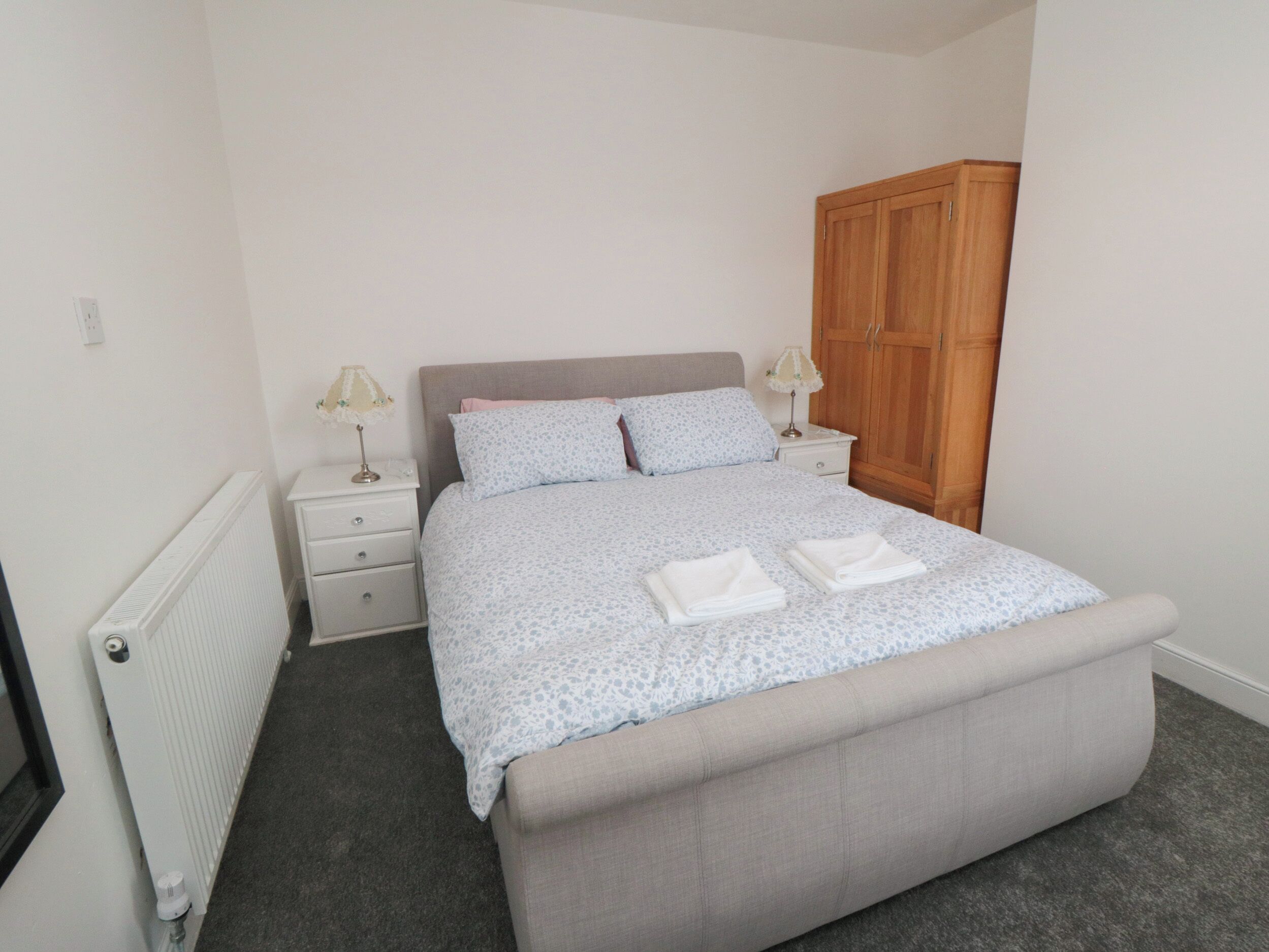 A bedroom with a bed, nightstands, a wooden wardrobe, and a radiator.