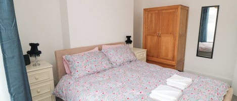 A bedroom with a bed, a wardrobe, a nightstand, a lamp, and a mirror.