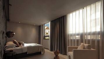 Une chambre à coucher moderne avec un lit, une chaise, une petite table et une fenêtre avec des rideaux.