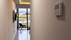 En hall med ett jämnt golv, ett väggmonterat säkerhetssystem och en dörr som leder ut till ett utomhusområde med en bänk.