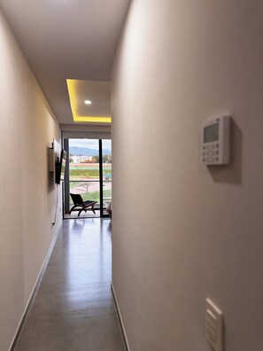 Ein Flur mit ebenem Boden, einem an der Wand montierten Sicherheitssystem und einer Tür, die zu einem Außenbereich mit einer Bank führt.