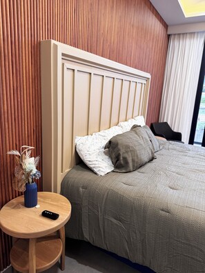 Ein Hotelzimmer mit einem Bett, einem runden Holztisch mit einer Vase und einer Fernbedienung, sowie einem Blick ins Freie durch ein Fenster.