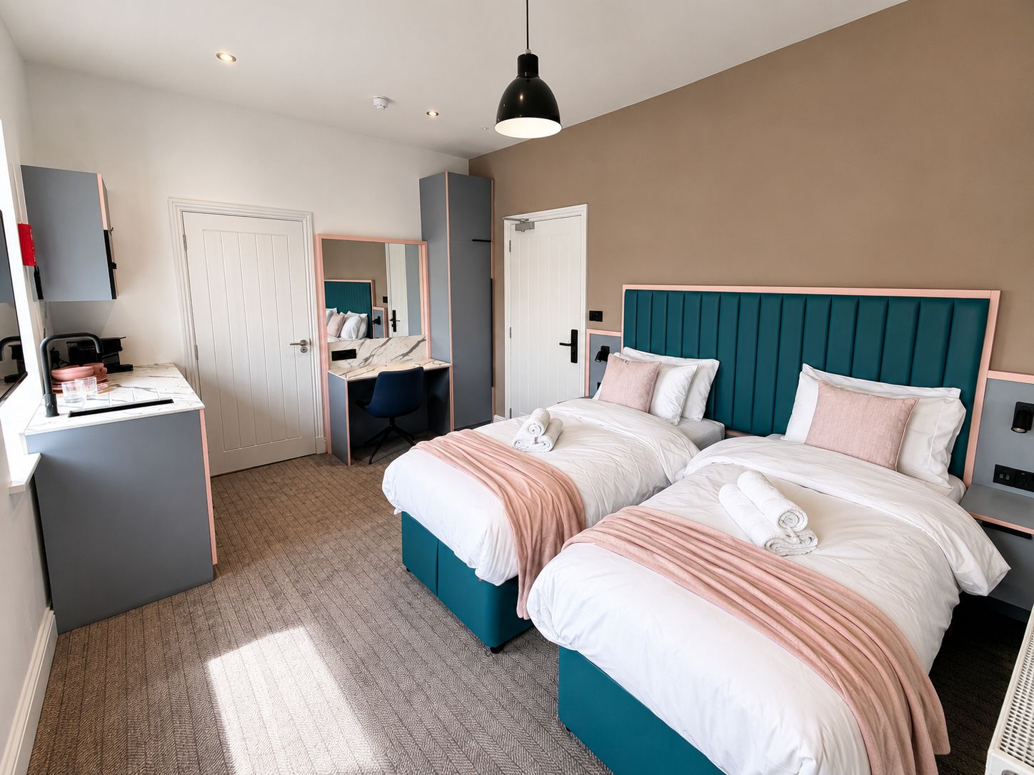A hotel room with two beds, a desk, a chair, and a wardrobe.
