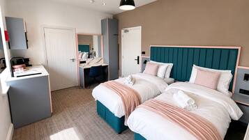 A hotel room with two beds, a desk, a chair, and a wardrobe.