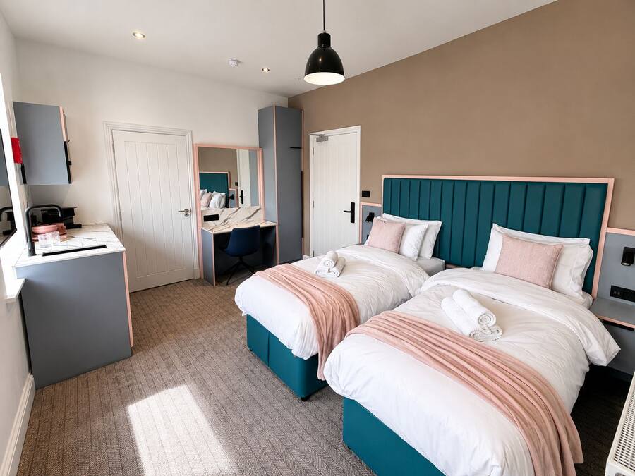 A hotel room with two beds, a desk, a chair, and a wardrobe.