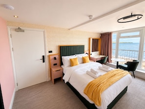 Habitación de hotel con cama, mesita de noche, silla y vista al mar.