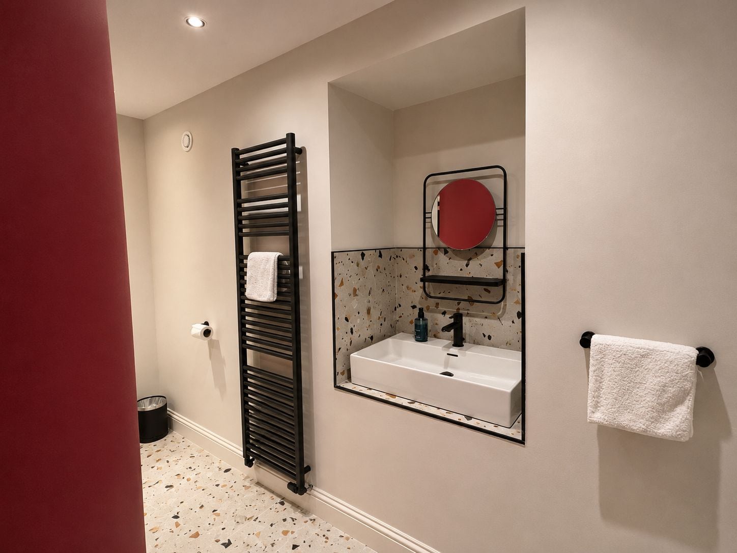 A bathroom with a freestanding towel rack, a sink with a mirror above it, and a patterned floor.