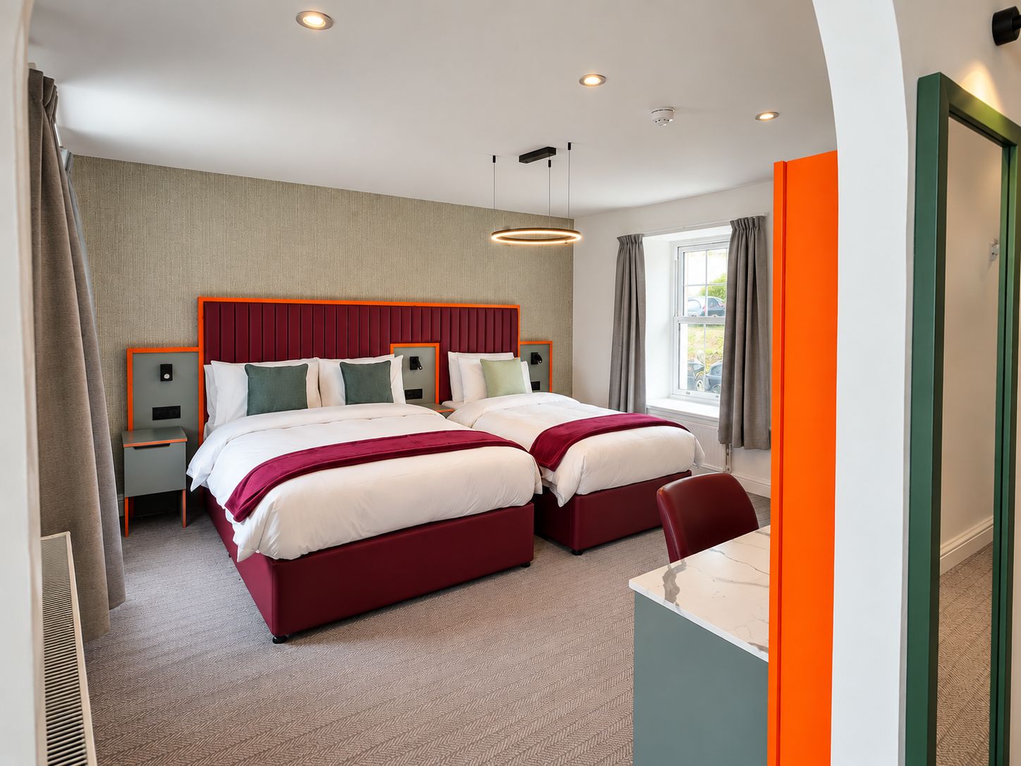 A hotel room with two beds, a desk, and a window with curtains.