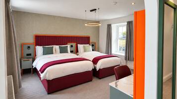 A hotel room with two beds, a desk, and a window with curtains.