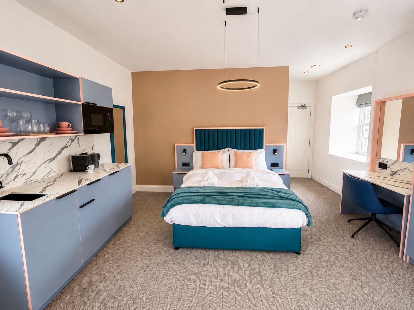 Una habitación de hotel moderna con cama, escritorio, kitchenette y un ventanal grande.