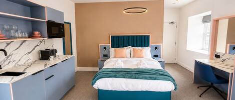 Una habitación de hotel moderna con cama, escritorio, kitchenette y un ventanal grande.