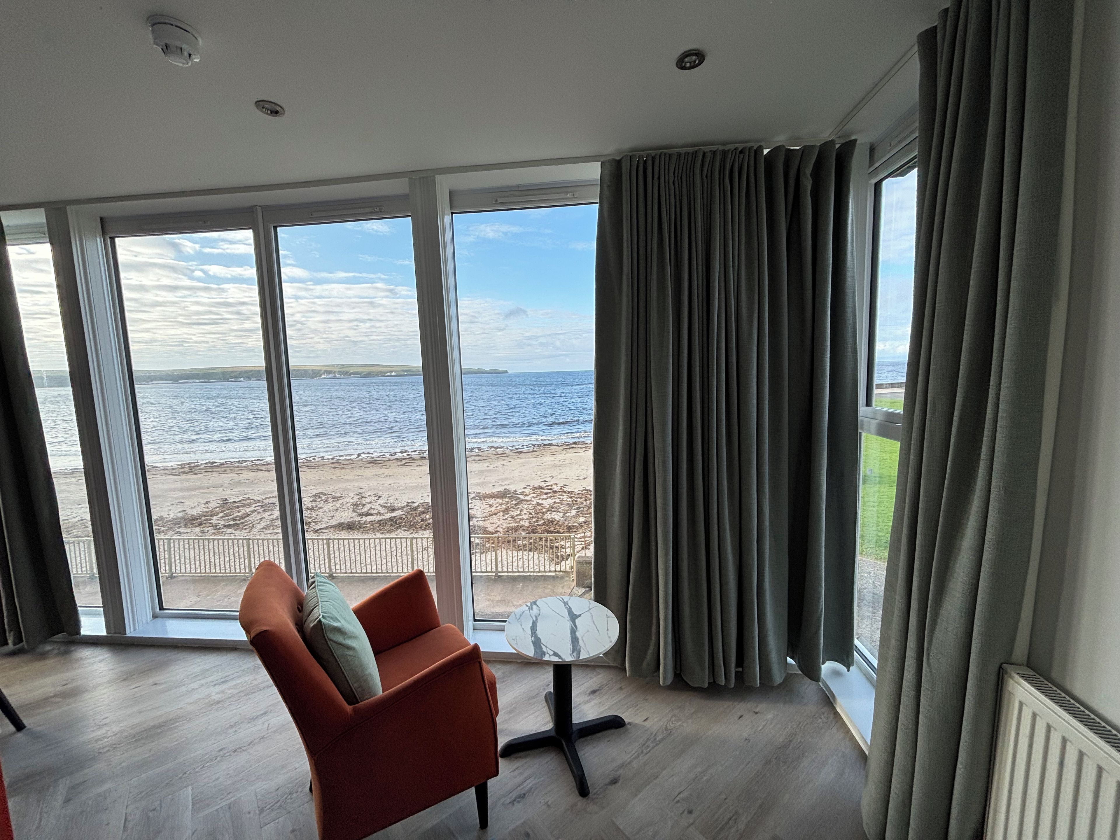 Ein Zimmer mit großem Fenster und Meerblick, ein Stuhl und ein kleiner Tisch.