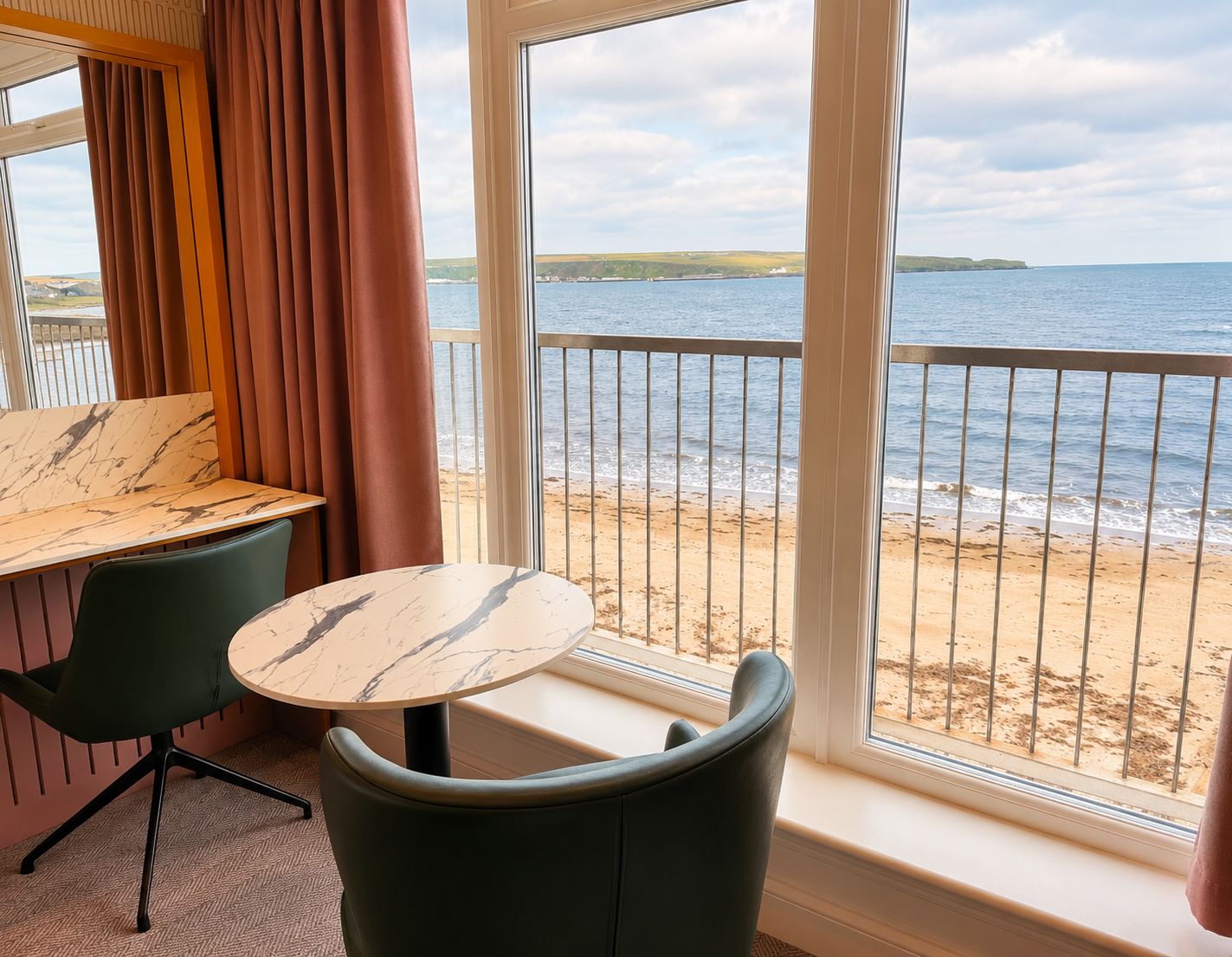 A room with a view of the beach, a table, and two chairs.