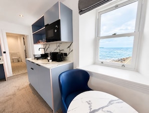 Una cocina compacta con vista al mar, una silla azul y una encimera de mármol.