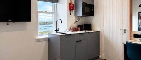 Een knus hotelkamer met een bed, een kleine kitchenette, een televisie en een raam met uitzicht op zee.