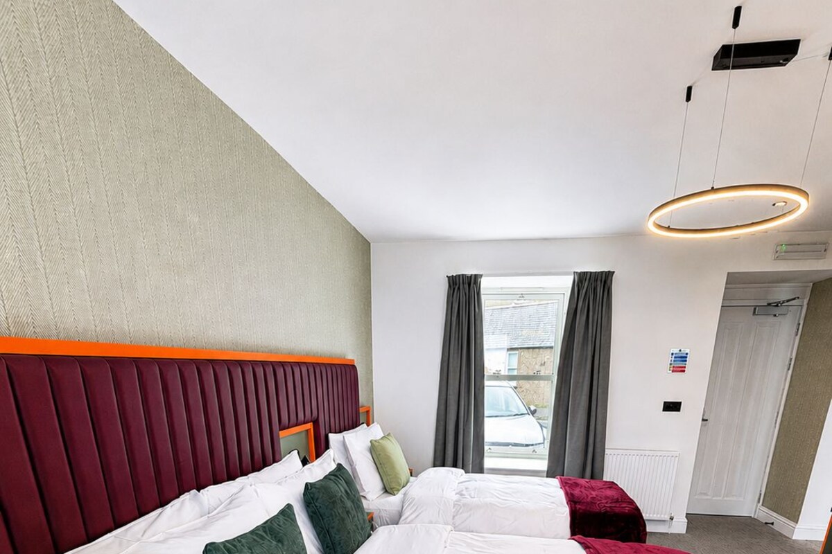 A hotel room with two beds, a headboard, a desk, and a view of the outside.