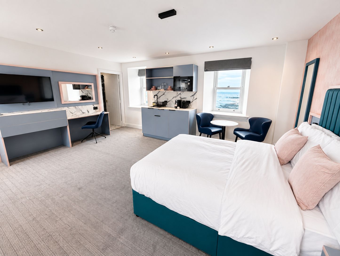 A modern hotel room with a bed, desk, and seating area.