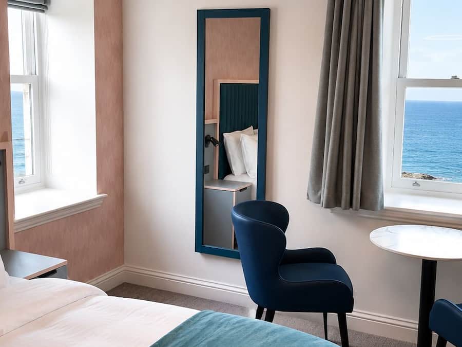 Habitación de hotel con cama, escritorio, silla, espejo y vista al mar.