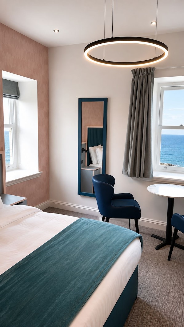 Habitación de hotel con cama, escritorio, silla, espejo y vista al mar.