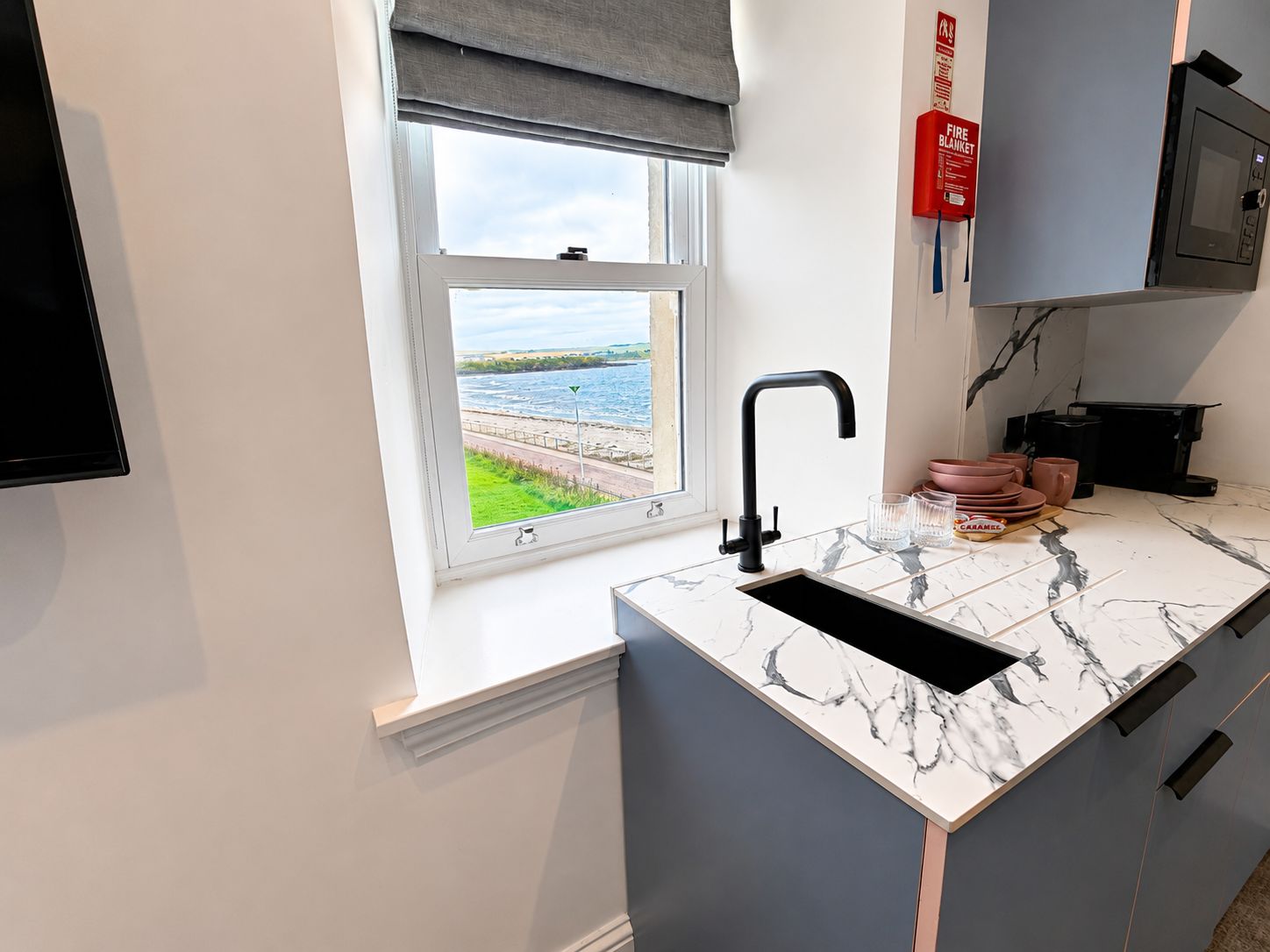 Una cocina moderna con un lavamanos integrado, una ventana con vista al mar y un detector de incendios en la pared.