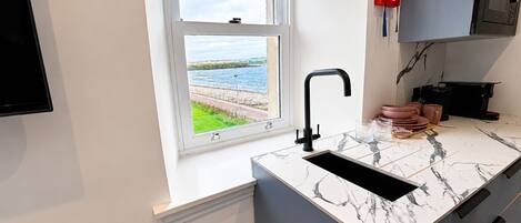 Una cocina moderna con un lavamanos integrado, una ventana con vista al mar y un detector de incendios en la pared.
