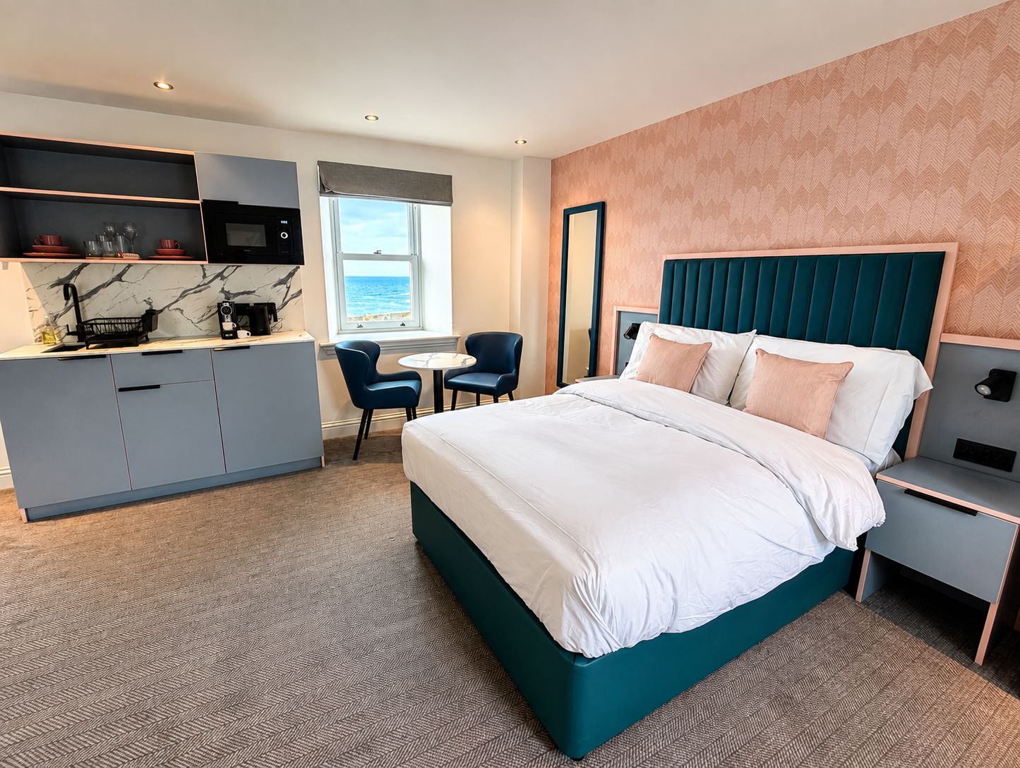 A hotel room with a bed, a desk, a chair, and a kitchenette.