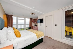 A hotel room with a bed, a desk, a television, and a balcony with yellow chairs.