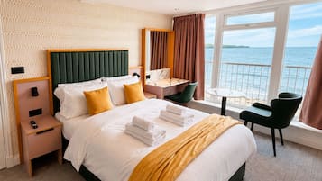 Quarto de hotel com uma cama, mesas de cabeceira, uma escrivaninha e vista para o mar.