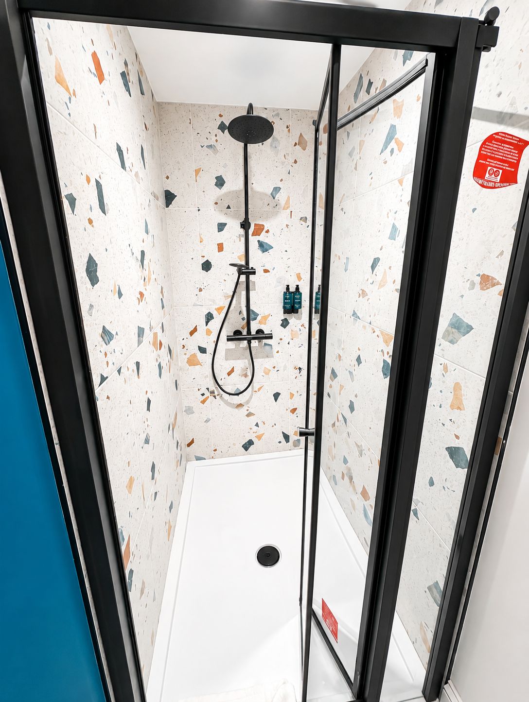 A glass-enclosed shower stall with a handheld showerhead, a handheld shower attachment, and a wall-mounted faucet.