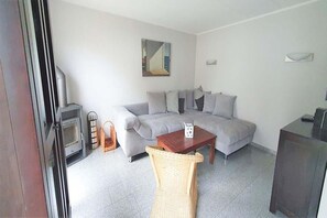 A living room with a sofa, a small table, a wicker chair, a fireplace, and a cabinet. - Familienfreundliches Ferienhaus mit Garten im Hafendorf Müritz (Rechlin)
