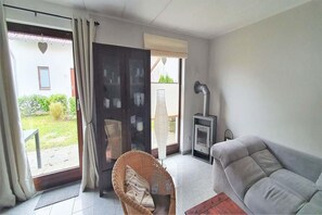 A room with a sofa, a wicker chair, a fireplace, and a sliding glass door leading to a patio. - Familienfreundliches Ferienhaus mit Garten im Hafendorf Müritz (Rechlin)