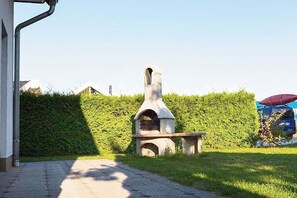 Ein Backofen aus Stein im Freien, ein gepflasterter Weg und ein Hecken entlang eines Gartens.
