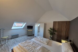 Ein Schlafzimmer mit Dachfenster, einem Bett, einem Kleiderschrank, einem Schreibtisch und einer Zimmerpflanze.
