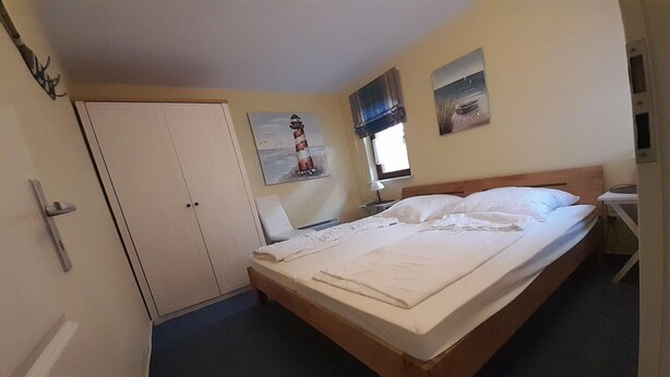 Ein Schlafzimmer mit einem Einzelbett, einem Kleiderschrank, einem Nachttisch und einem Fenster.