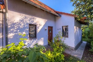 Ein eingeschossiges Gebäude mit weißer Fassade, einer braunen Tür und zwei Fenstern.