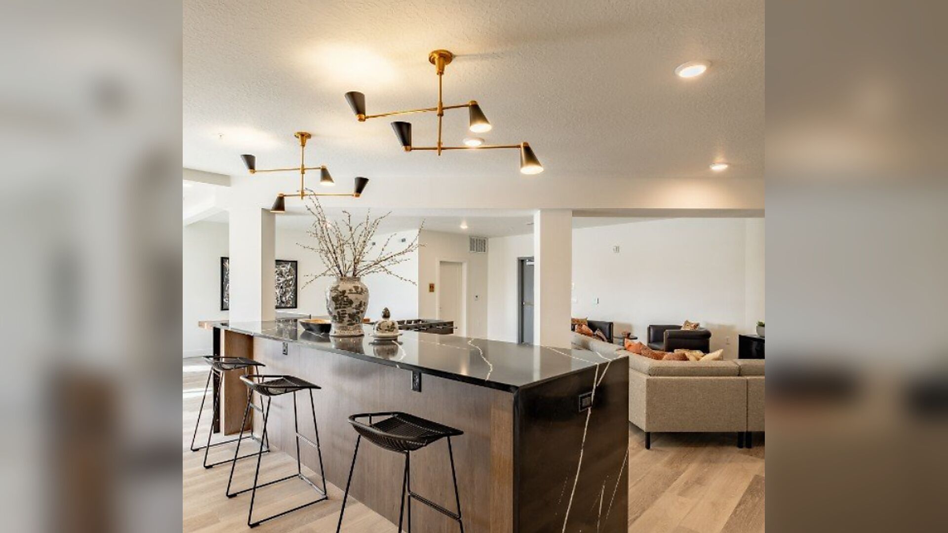 A modern kitchen with a central island, bar stools, pendant lighting, and a view into the living area.