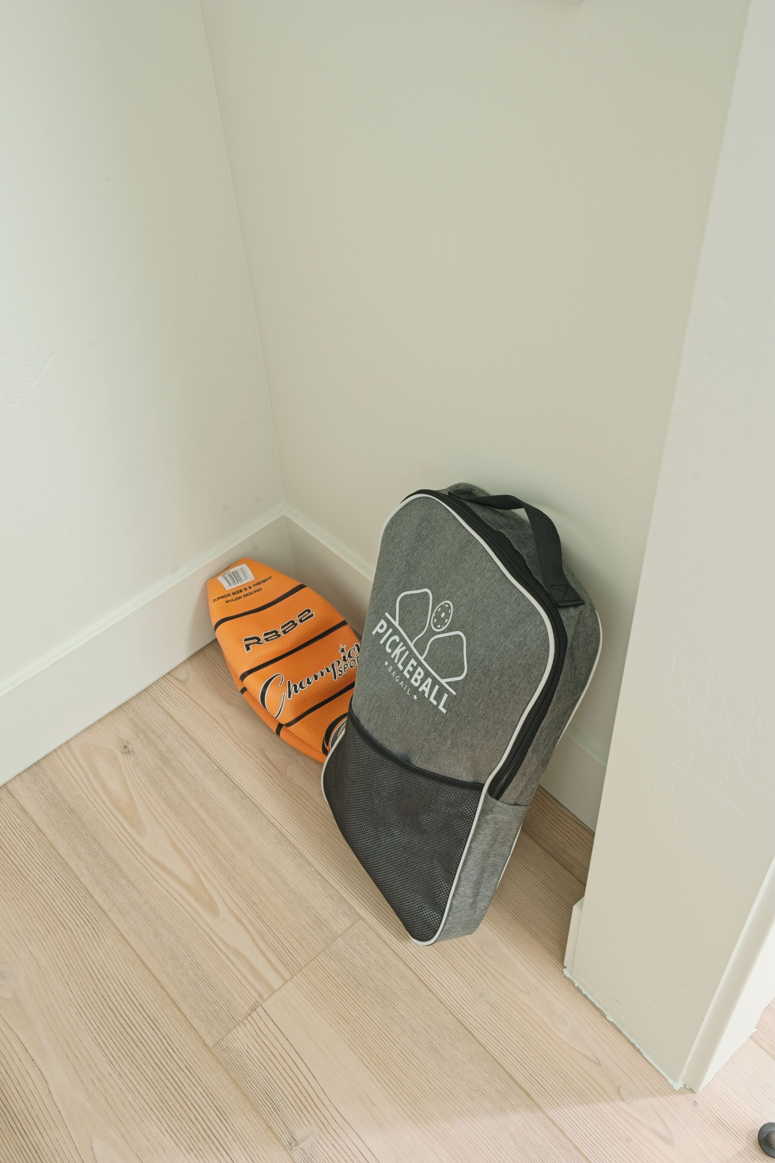 Een hoek van een kamer met een grijze tas waarop 'Pickleball' staat en een oranje tas met 'Champion' erop.
