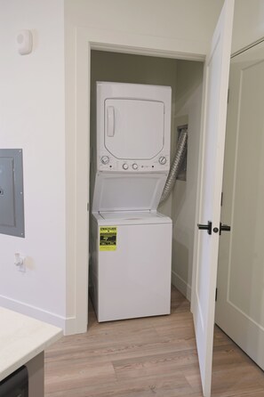 A compact, white laundry room with a front-loading washing machine, a visible energy efficiency label, and a door leading to another room.