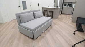En modern lägenhet med en grå soffa, ett litet kök och ett trägolv.