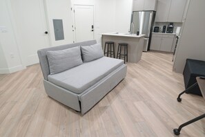 A modern apartment with a grey sofa, a kitchenette, and a wooden floor. - Modern Studio Near Airport with Free Parking (Millcreek)