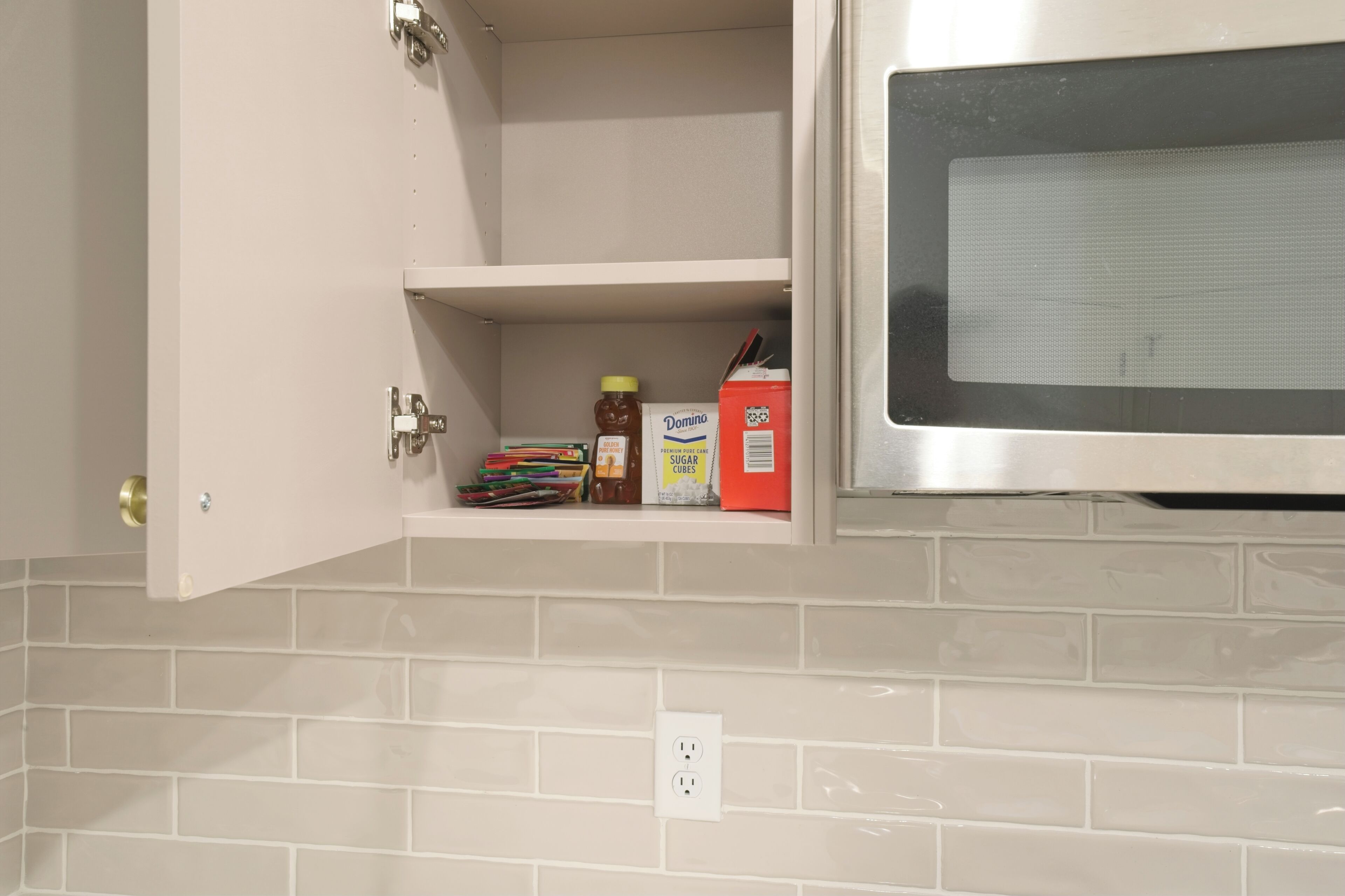 A kitchen with a microwave, a shelf with various items including a honey jar, sugar cubes, and a box of Domino sugar.
