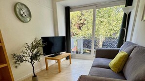 A living room with a sofa, a TV on a stand, a potted plant, and a balcony with a view. - House Sleeps 8 With Balcony (London)