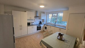 A compact kitchen with white cabinets, a microwave, oven, and a washing machine. - House Sleeps 8 With Balcony (London)