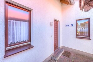 A building with a window with a curtain, a door, and a number sign. - Geräumiges Ferienhaus für Familie im Hafendorf Müritz Rechlin (Rechlin)