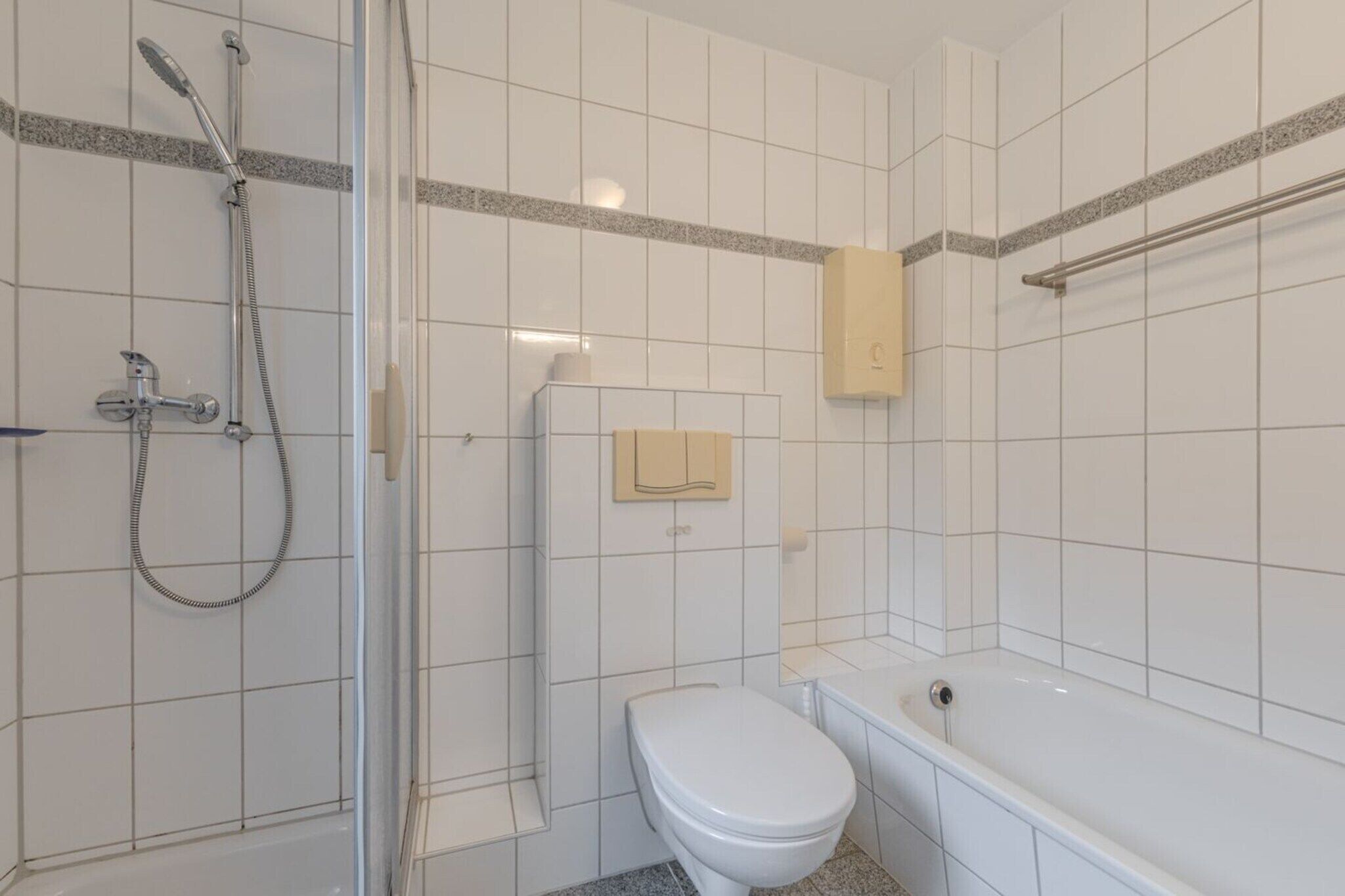 Baño con ducha, inodoro y bañera, paredes con azulejos y un perchero para toallas.