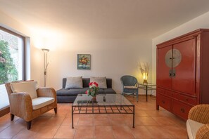 A living room with a sofa, two wicker chairs, a glass coffee table with a vase, a red cabinet, and a painting on the wall. - Geräumiges Ferienhaus für Familie im Hafendorf Müritz Rechlin (Rechlin)