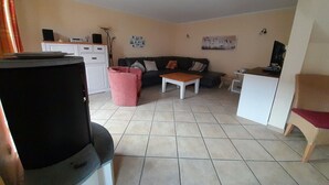 Un salón con sofá, mesa de centro, televisor y una zona de cocina con armarios y encimera.