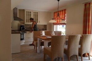 A kitchen with a dining area, including a table with chairs, a hanging light fixture, and a window with curtains. - Gemütliches Ferienhaus mit Terrasse nahe dem Müritzsee in Rechlin (Rechlin)