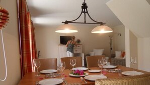 Comedor con mesa de madera dispuesta para cuatro personas, sillas de mimbre y una araña.